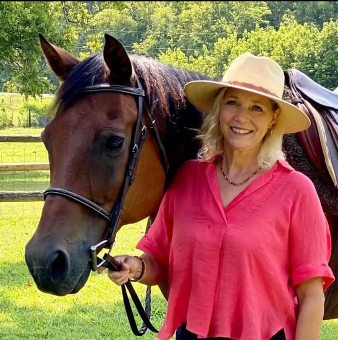 A woman standing next to a horse in the grass.