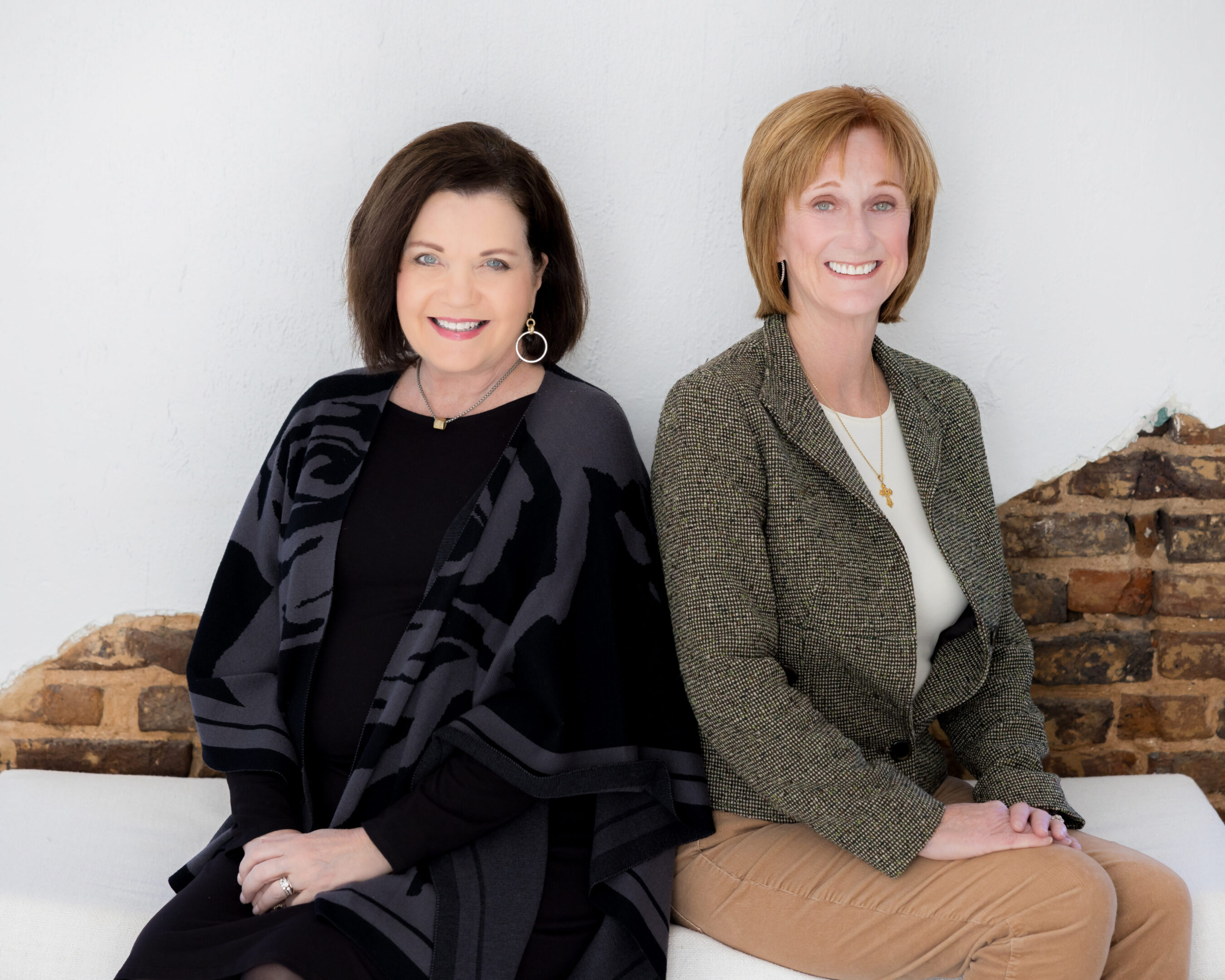 Two women sitting on a bench posing for the camera.