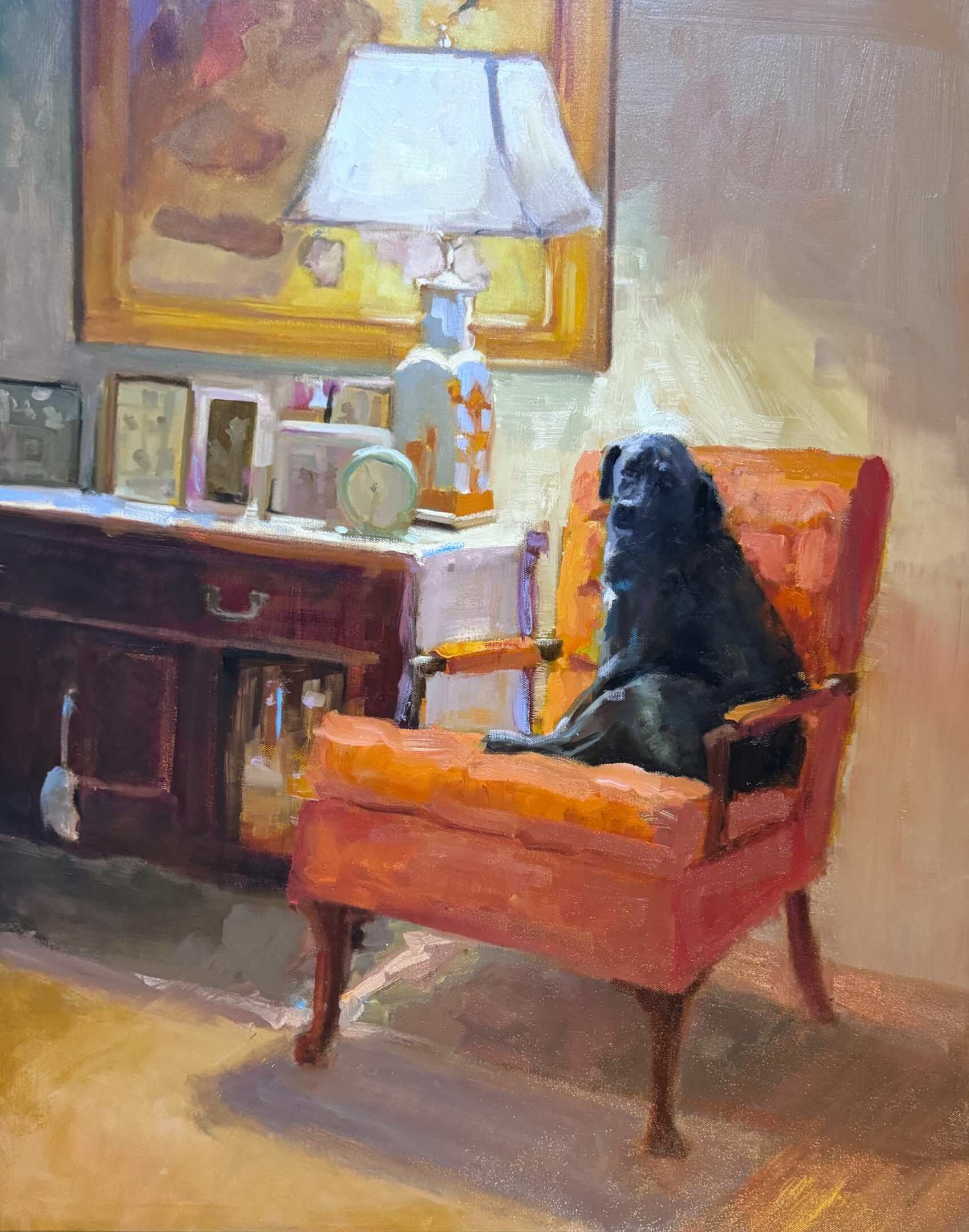 A black dog sitting on an orange chair in front of a lamp.