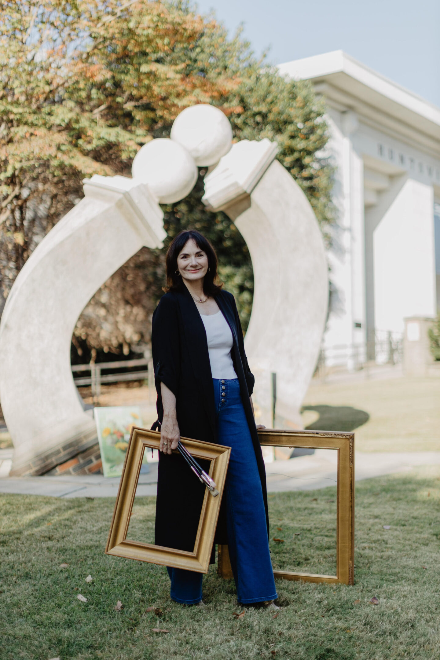 A woman holding two frames in front of an arch.